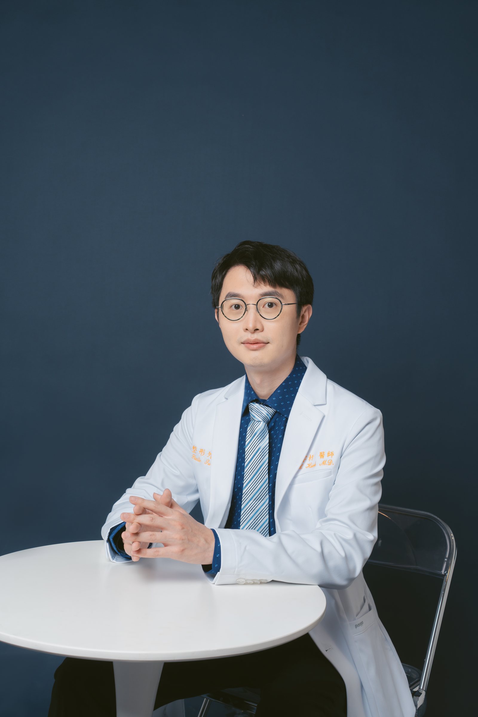 謝宇軒醫師身穿白袍,坐在白色圓桌前雙手交握